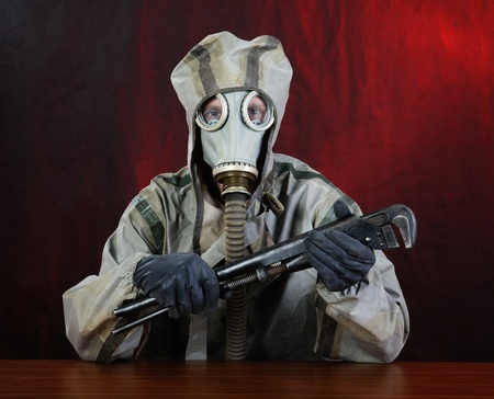 Person in chemical protection suite holds a wrench.