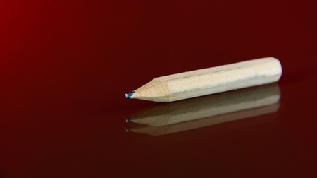 Old pencil on dark red background. Single object
の写真素材
