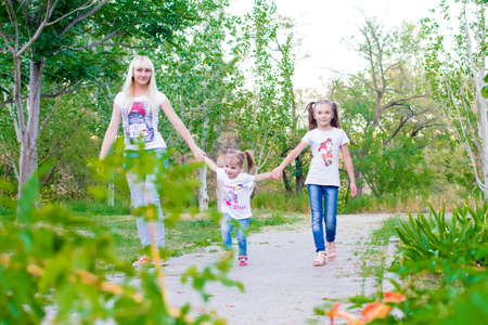 Young mother and two daughters walking in summer park. They are happy. In girls, funny hairstyles. People dressed in jeans and T-shirts.の写真素材