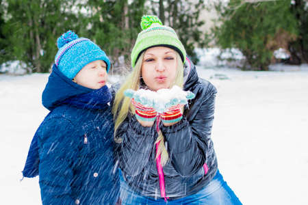 Happy little cute baby and mother on a sunny winter day playing with the snow and blowing snow onの写真素材