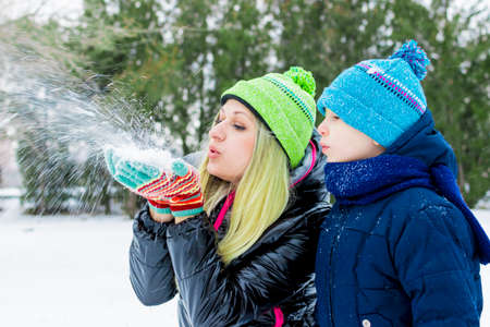 Happy little cute baby and mother on a sunny winter day playing with the snow and blowing snow onの写真素材