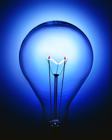 Close up of a glowing incandescent light bulb on blue backgroundの写真素材