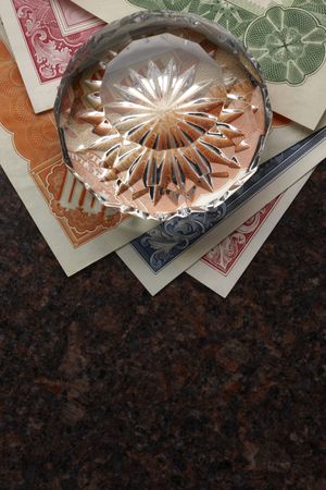 Stock certificates and faceted crystal paperweight shot on granite surface