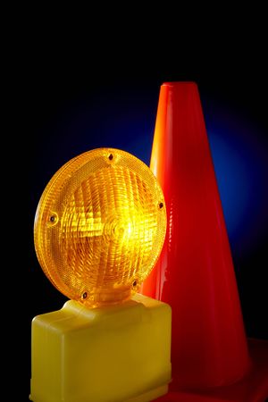 Yellow warning light and orange road cone shot on dark background