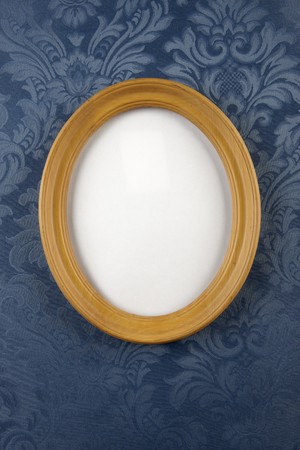 light wood, oval picture frame shot on blue, floral, flocked wall paper with space for photograph to be inserted and room for copyの写真素材