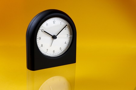 Modern, black alarm clock shot on yellow-orange background with reflection and space for copy