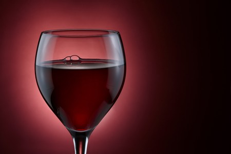 Glass of red wine shot on rich burgundy background with space for copyの写真素材