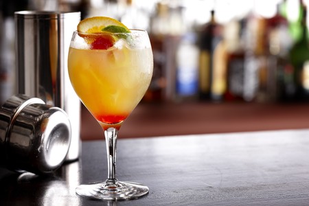Cool, colorful summer drink with orange, lime and cherry, shot in bar with shaker