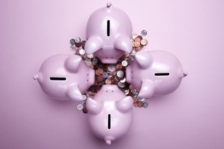 4 pink piggy banks and a pile of coins shot on pink bacgroundの写真素材