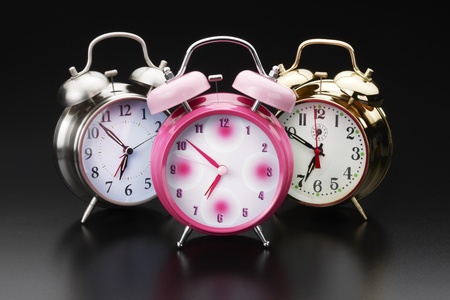 3 colorful, classic alarm clocks shot on reflective surface