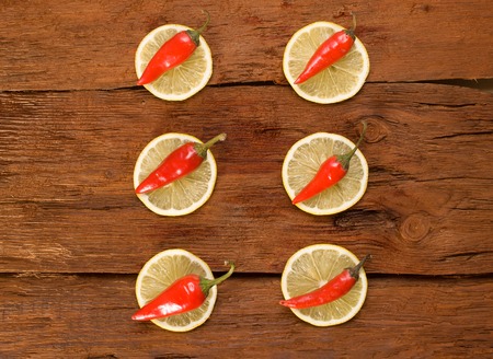 Red chili pepper, slices a lemon on brown cutting board.の写真素材