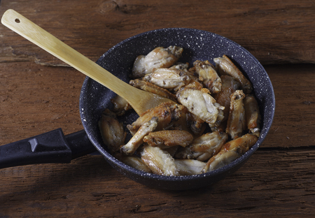 Fried chicken wings in frying pan with wooden spatula. Homemade food.の写真素材