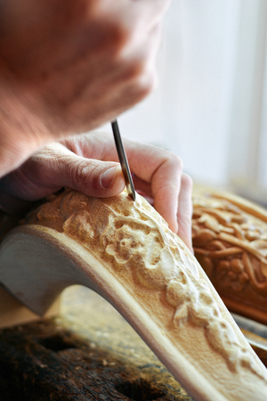 Artisan woodcarver creates a furniture ornament. Woodcarver's hands, chisels, tools, wood-carved part of a classic style chair.の写真素材