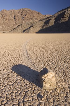 The phenomenon of the moving rocks at Death Valley Race Track Playa. The setting sun casts a shadow over the near by rock, still basking the mountains in the background in a warm glowの写真素材