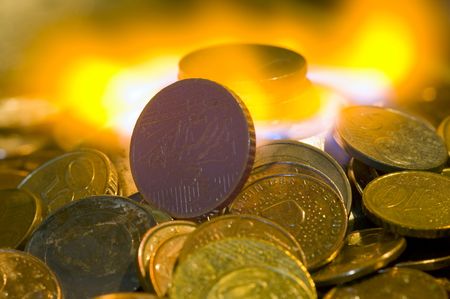 A glowing red hot coin in front of the blue flames of burning natural gas, a metaphor of wasting energy, not only bad for the environment, but also a waste of moneyの写真素材