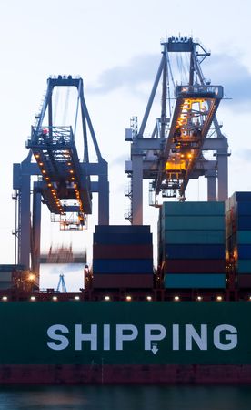 The continuous loading with two huge cranes of a sea going cargoship during twillight hour.の写真素材