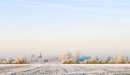 The soft, sun-lit polders and view on the church of Ellewoutsdijk, Zeeland, The Netherlands on a cold, hoarfrosted morningの写真素材