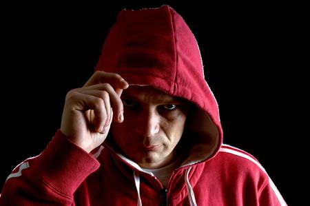 A grim looking hooligan, lifting his hood with his right arm, glaring at the camera.