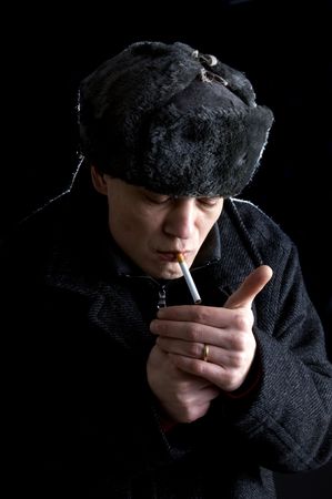 A man, dressed in Soviet attire, lighting a cigaretteの写真素材