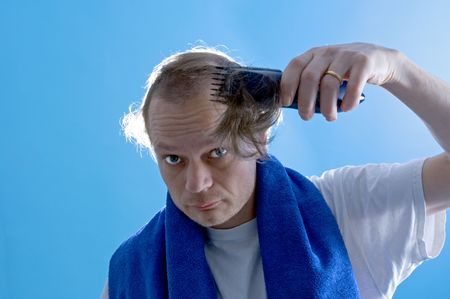 A middle aged man dressed in a white t-shirt, shaving his own hair with a clipper