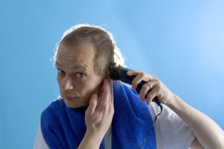 A middle aged man dressed in a white t-shirt, shaving his own hair with a clipper