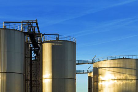 An industrial plant with huge stainless steel silos, reflecting in the evening sun