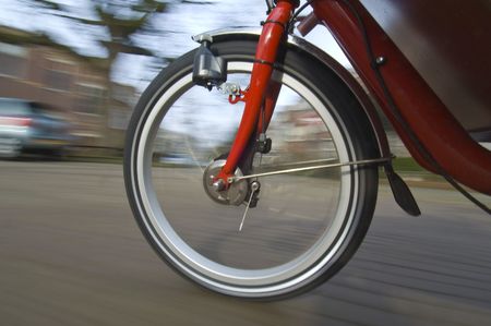 The spinning and vibrating wheel of a delivery bicycle on a suburban street