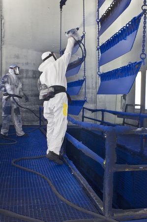 Two workers, manually spray painting steel objects using professional equipment, and using proper safety attire and ventilated masksの写真素材