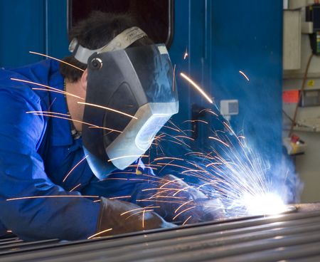 A welder, wearing a protective helmet and fire retardant clothing, working on steel beams