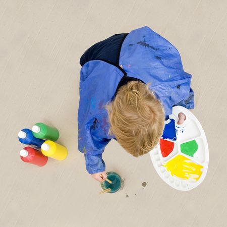 A small boy, crouching down to rinse a brush which he used with poster paint for a painting on a huge cardboard surfaceの写真素材