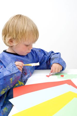 Child pasing pieces of colored paper, using a brush with glueの写真素材