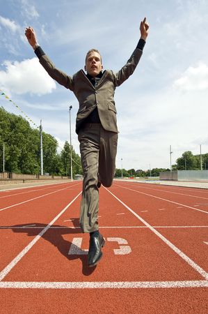 Metaphore for success in business - a business man crossing the finish line on an athletics track with his arms raised in victoryの写真素材