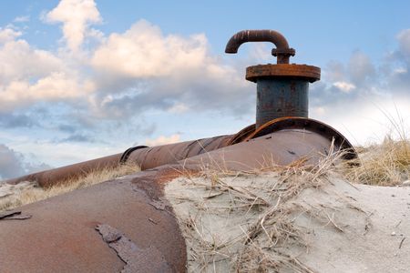 An old, obsolete pipeline with a faucet and flanges, surrounded by the drift-sand and marram grass of the dunes against a radiant cloudscape.の写真素材