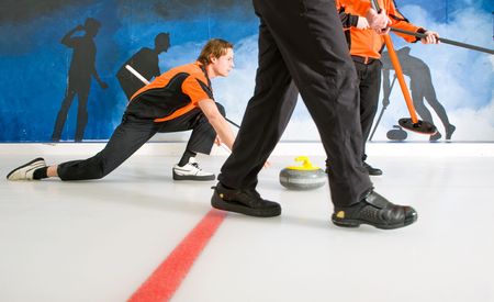 Curler, gliding on the ice, delivering a stone, with two sweepers, to act on the Skip's requestの写真素材