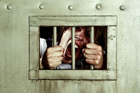 Cross-processed image of a man going insane, grabbing the bars of his jail cell, looking rabit and screaming uncontrollablyの写真素材