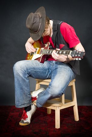 A musician wearing an old, leather hat, playing on his guitar whilst sitting on a stoolの写真素材
