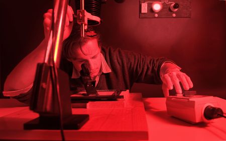 Photographer working in a darkroom, printing analogue negatives with an enlarger, fine-tuning the focus of the image on the easel with a scope, hands on the exposure timerの写真素材