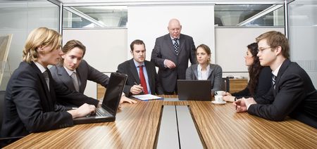 Seven people in a cubicle, preparing for a management team meeting