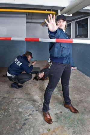 Policewoman making a stopping gesture with a blood stained outstretched hand to keep a bystander away from the perimeter of a crime sceneの写真素材