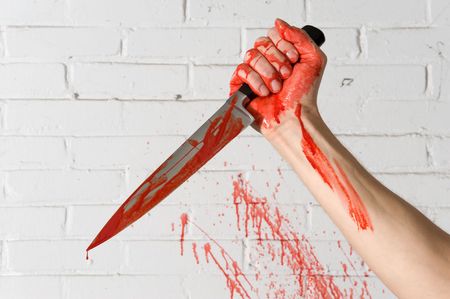 Blood covered knife, still dripping, in the hands of a murderer, with blood spatter on the brick wall.の写真素材