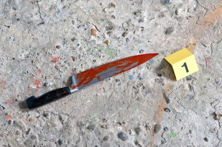 Crime scene photo of a blood covered knife - the murder weapobn - at a crime scene with a placard...
