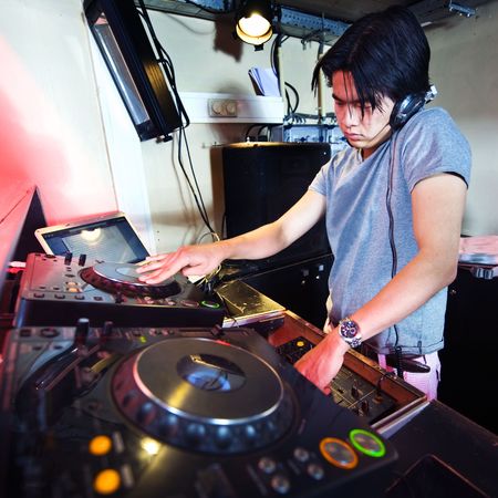 Disc Jockey at work in his booth in a nightclub, mixing and scratching with headphones.