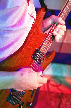 Looking over the shoulder of a guitarist at his hands, on a stage in a discotheque