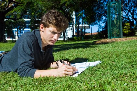 Young college student doing his homework in the park on a sunny dayの写真素材