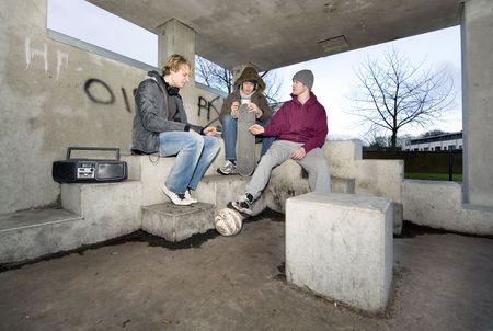 Three adolescent youths lighing cigarettes in a shelter in a suburbian areaの写真素材