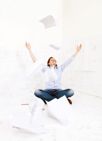 Engineer, surrounded by technical drawings, tosses a stack of papers into the air, illustrating the immense work pressure he's underの写真素材
