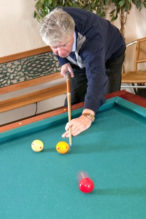 Senior man playing carambole billiards - slight motion blur in the red and yellow billiard balls