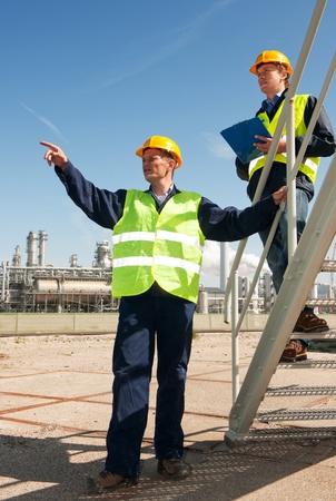 A worker discussing procedures with another worker in front of a petrochemical refineryの写真素材