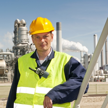 Engineer poses casually in front of a refinery, wearing a safety vest and hard hatの写真素材