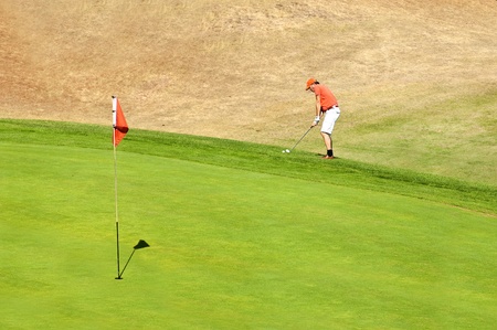 Golf player using a wedge to put his ball on the green near the holeの写真素材